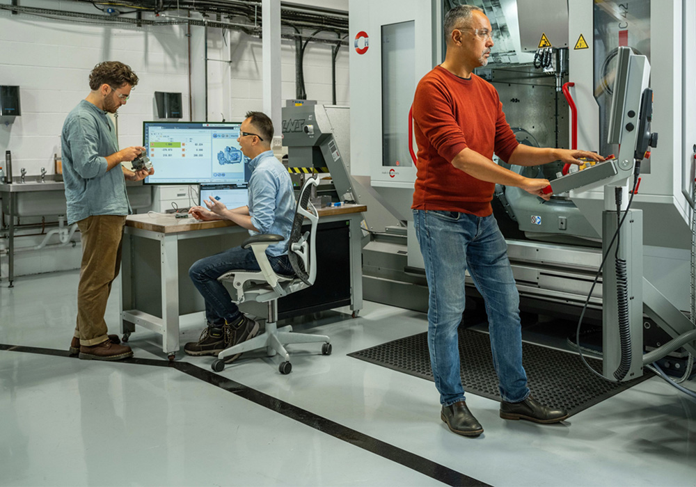 3 men situated in a advanced machining environement with precision equipment, showcasing innovation in manufacturing workflows